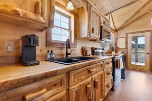 A wooden kitchen with a built-in oven, a coffee machine, and a sink. - Firelight Cabin | Loft + 2 Baths | Sleeps 8 (Fredericksburg)