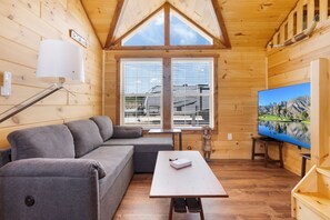 A wooden cabin interior with a sofa, a table, and a TV. - Firelight Cabin | Loft + 2 Baths | Sleeps 8 (Fredericksburg)