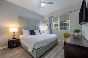 Ein modernes Schlafzimmer mit Bett, Nachttischen, Schreibtisch, Stuhl, Deckenventilator und einem Fenster mit Jalousien.