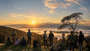 Een groep mensen op een grasheuvel met uitzicht op een vallei, tijdens zonsopkomst of zonsondergang.