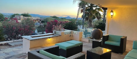 A terrace with wicker furniture, a decorative sphere, and a view of the landscape.