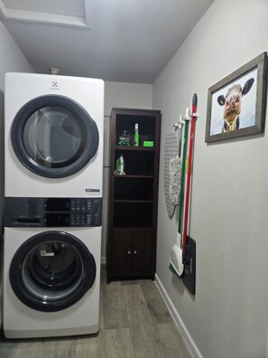 Une buanderie équipée d’un lave-linge et d’un sèche-linge à chargement frontal, d’un meuble en bois contenant des produits de nettoyage et d’un tableau représentant une vache accroché au mur.