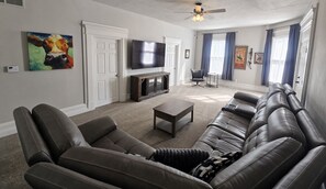 A living room with a large leather sofa, a coffee table, a flat-screen TV, and a ceiling fan.