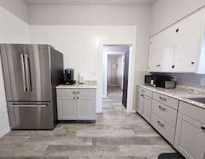 A modern kitchen with stainless steel appliances, white cabinetry, and a wooden floor.