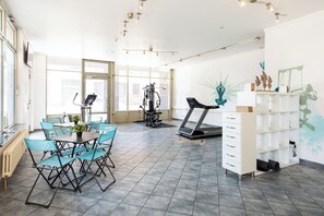 Ein geräumiges Zimmer mit Esstisch, Stühlen, Laufband und einem weißen Schrank mit Regalen.