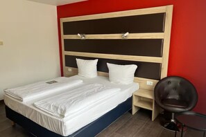 Ein Bett mit Holz-Kopfteil, zwei Kissen, ein Nachttisch und ein Stuhl.