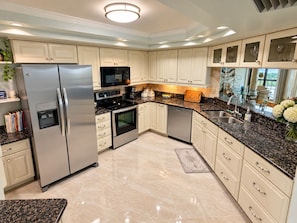 A modern kitchen with stainless steel appliances, white cabinetry, and a granite countertop. - Islandia II Cozy Beachfront 2BR Condo, Ocean & River Views, Hutchinson Island FL (Jensen Beach)