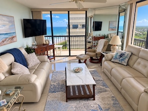 A spacious living room with a large window offering a view of the ocean and a balcony.