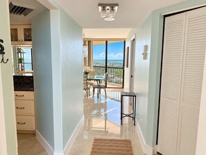 A hallway with a view to a balcony, a dining area, and a kitchen. - Islandia II Cozy Beachfront 2BR Condo, Ocean & River Views, Hutchinson Island FL (Jensen Beach)