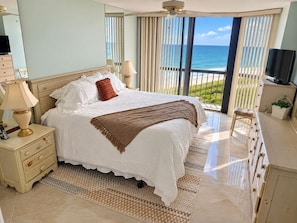 A bedroom with a large bed, a TV, a dresser, and a view of the ocean. - Islandia II Cozy Beachfront 2BR Condo, Ocean & River Views, Hutchinson Island FL (Jensen Beach)