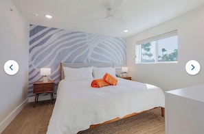 A bedroom with a large bed, two bedside tables with lamps, a window with a view, and a wall with a zebra print.