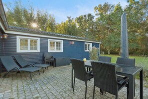 Ein blaues Haus mit Terrasse, Gartenmöbeln und einem hohen Obelisken.