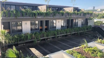 A modern building with multiple floors, large windows, and a rooftop garden with various plants.