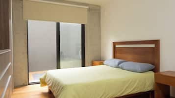 A bedroom with a bed, a wooden headboard, a nightstand, and a sliding glass door leading to a balcony.