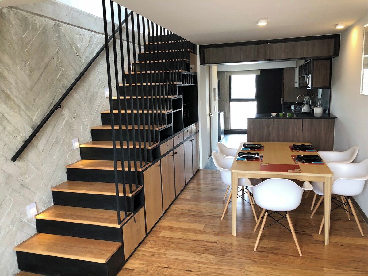 Eine moderne Küche mit Essbereich, einer Holztreppe und weißen Stühlen.