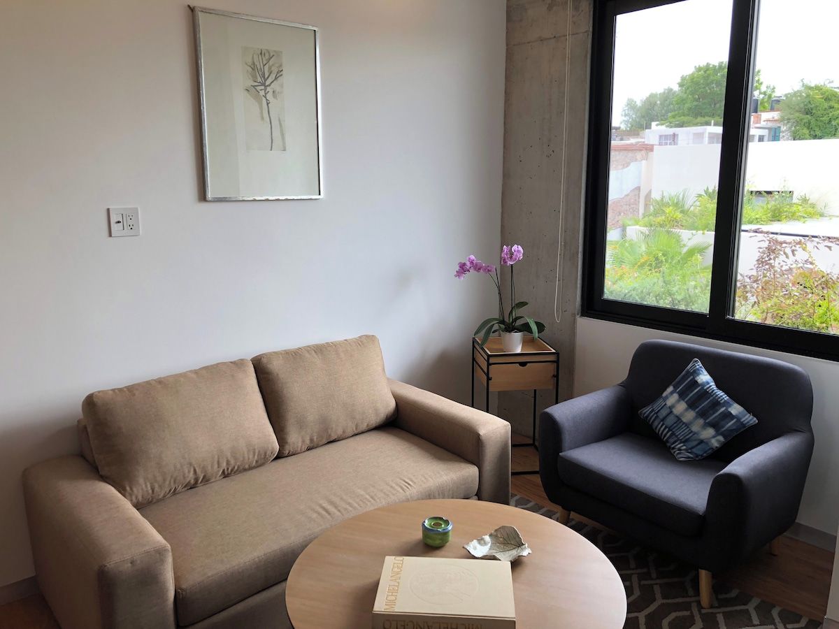 A living room with a sofa, armchair, coffee table, and a potted plant.
