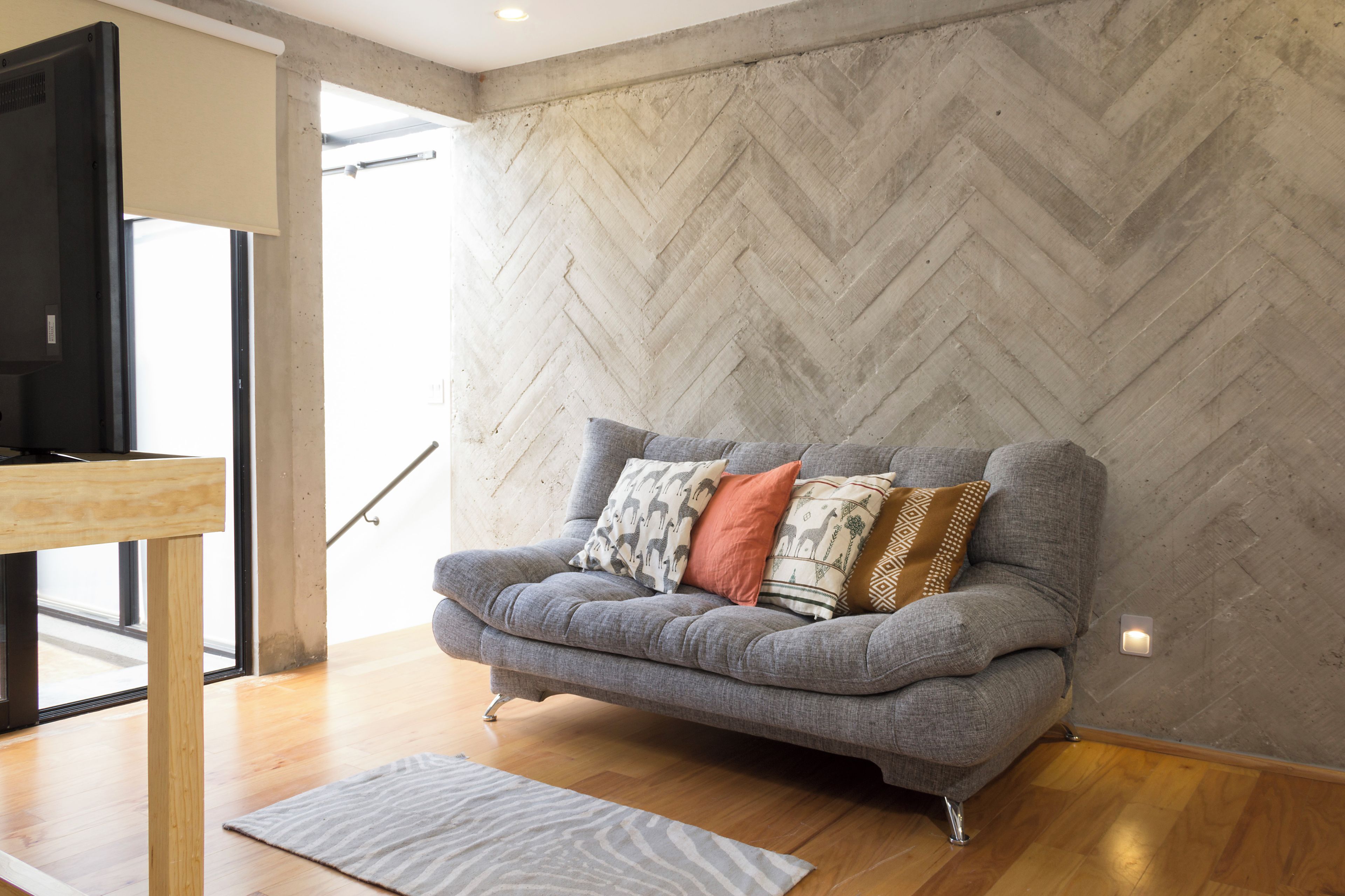 Un saló modern amb un sofà gris, coixins estampats, una taula baixa de fusta i una paret amb dibuix de punt de petons.