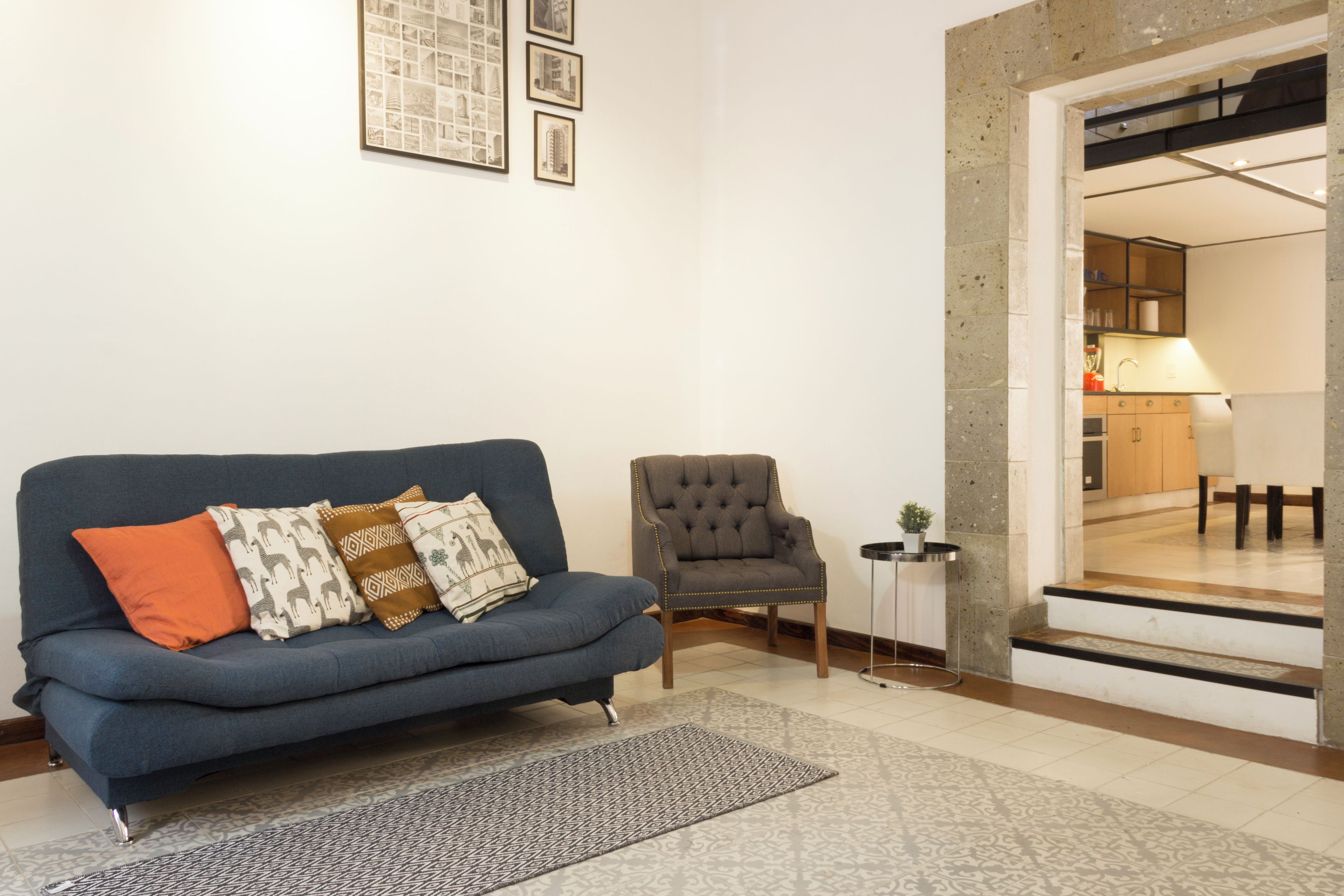 Una sala de estar con un sofá azul, un sillón gris, un tapete estampado y una pequeña mesita.