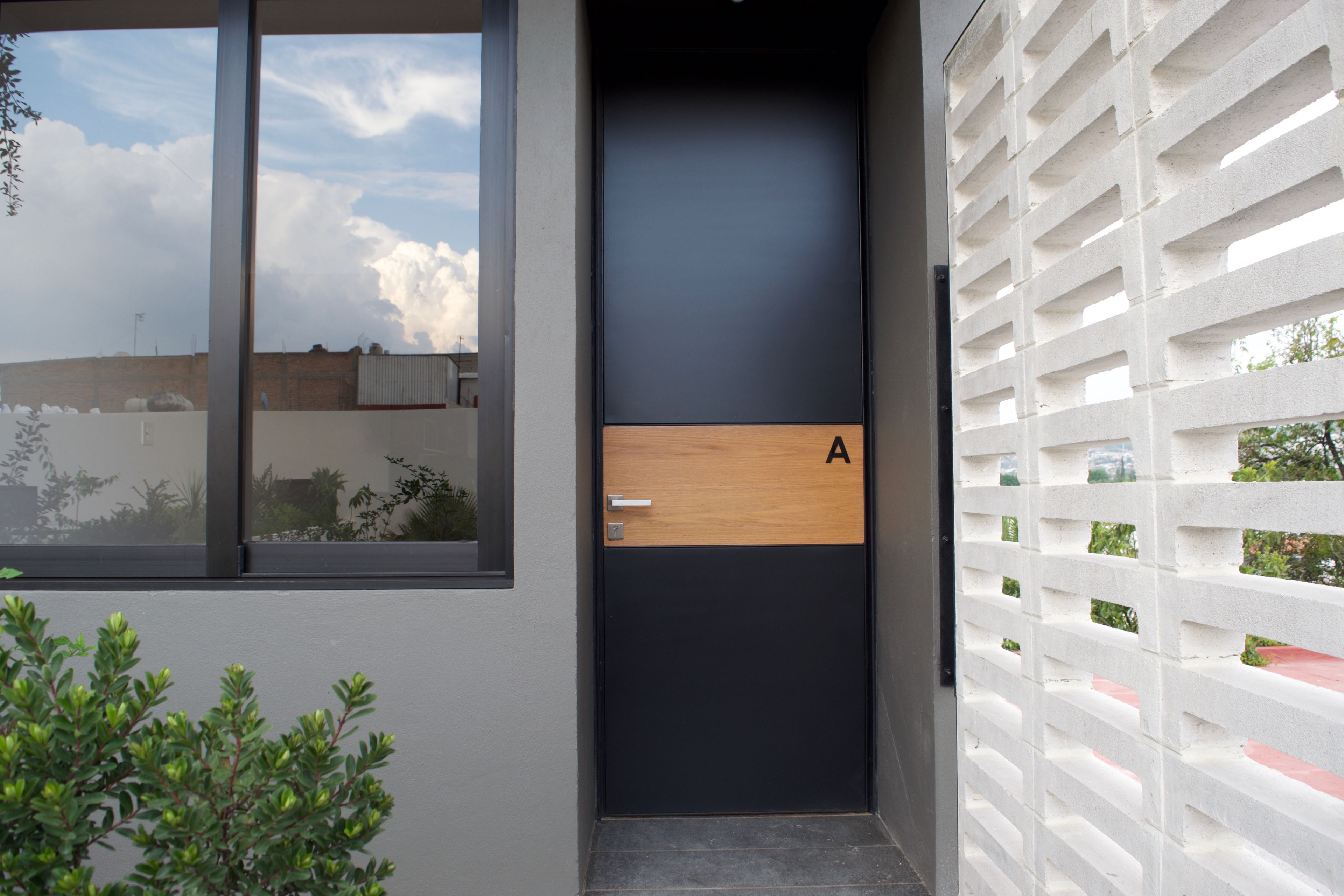 Una puerta moderna con paneles oscuros y claros, una sección de madera y un tirador de metal.