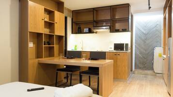 A compact kitchenette with a microwave, coffee maker, and a small refrigerator. There is a wooden dining table with chairs and a bed with a white blanket.