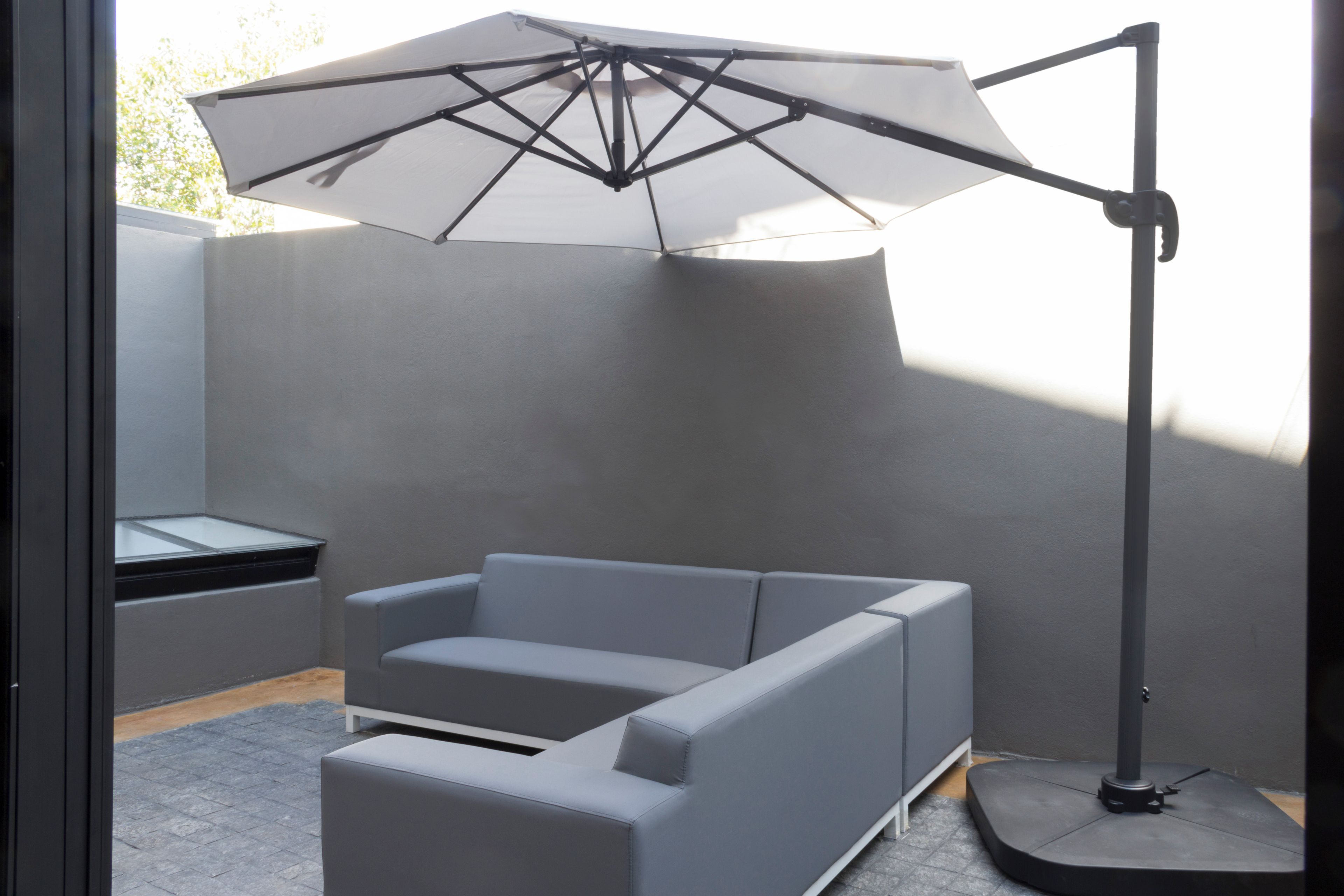 A modern outdoor seating area with a grey sofa and a large umbrella.