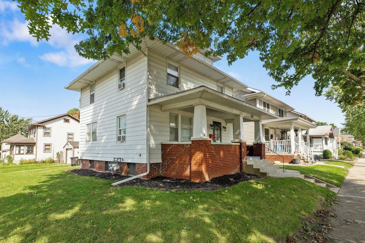 A two-story house with a front porch, a brick foundation, and a well-maintained lawn.