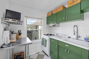 Una cocina con estufa a gas, armarios blancos y un ventanal.