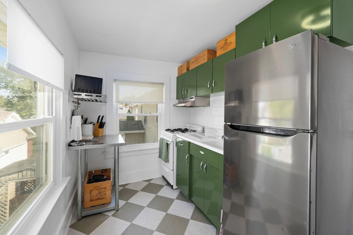 A kitchen with a stainless steel refrigerator, green cabinets, a window, and a checkered floor.