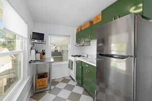 A kitchen with a stainless steel refrigerator, green cabinets, a window, and a checkered floor. - Charming 2BR Near Downtown Fort Wayne | Free Parking + In-Unit Laundry (Fort Wayne)