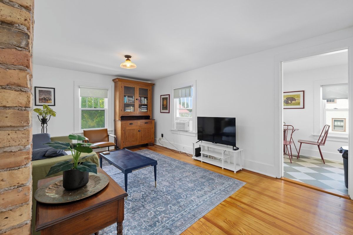 A living room with a television, wooden cabinet, and a dining area with chairs.