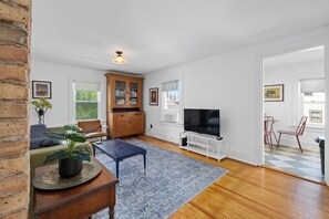 A living room with a television, wooden cabinet, and a dining area with chairs. - Charming 2BR Near Downtown Fort Wayne | Free Parking + In-Unit Laundry (Fort Wayne)