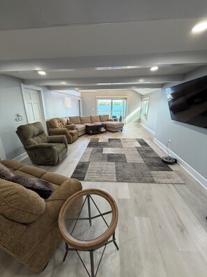 A spacious living room with a sectional sofa, a round wooden table, and a large flat-screen TV mounted on the wall. - Thompson Lake Presidential Penthouse (Otisfield)