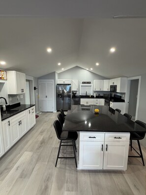 A modern kitchen with white cabinetry, a black countertop, and a central island with seating. - Thompson Lake Presidential Penthouse (Otisfield)