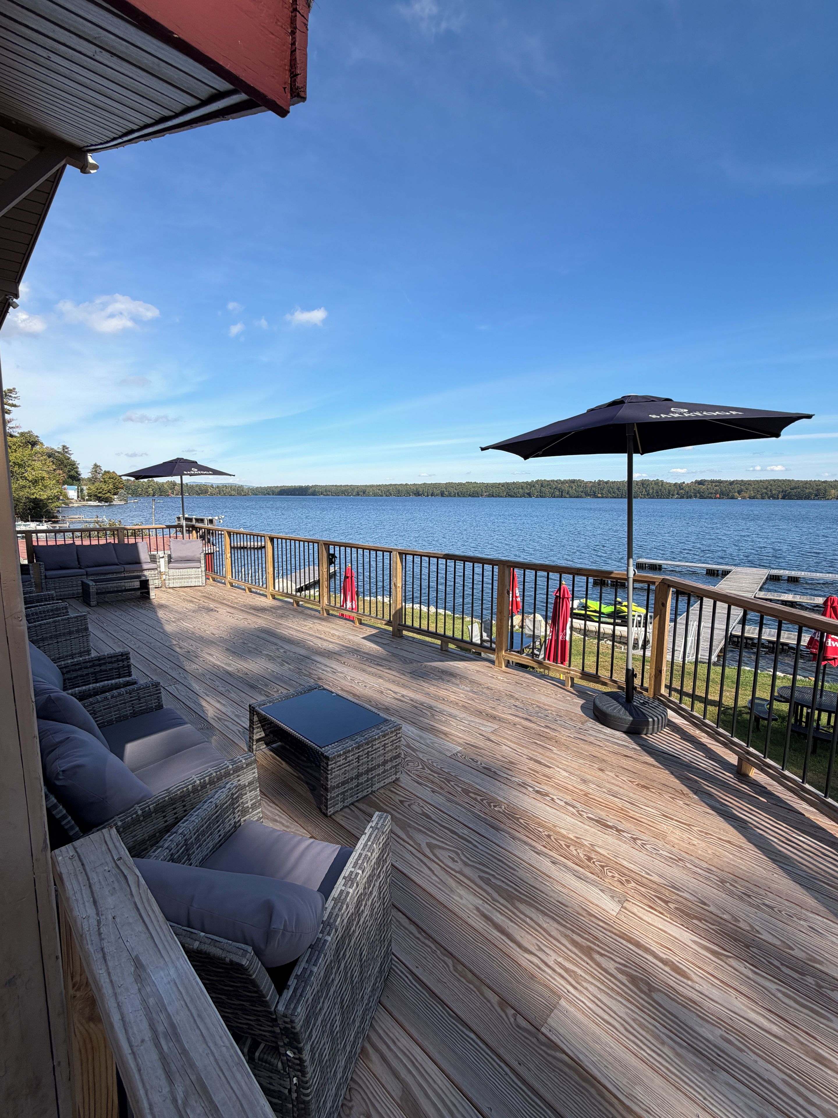 A deck with outdoor seating, a view of a lake, and a wooden railing.