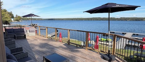 A deck with outdoor seating, a view of a lake, and a wooden railing.