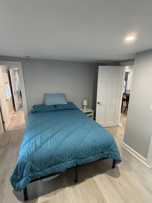 A bedroom with a bed, a nightstand, and a door leading to another room. - Thompson Lake Presidential Penthouse (Otisfield)