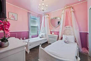 Ein zart rosa eingerichtetes Schlafzimmer mit zwei Betten, einer Kristallleuchter und einem spiegel mit Herzform.