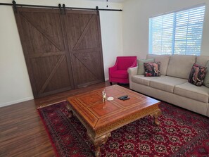 A living room with a sliding barn door, a red chair, a beige sofa with patterned cushions, a wooden coffee table, and a patterned rug.