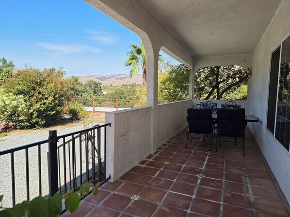 A covered patio with a table and chairs, a railing, and a view of the surrounding landscape.