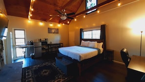 Ein gemütliches Schlafzimmer mit Bett, Schreibtisch und Stuhl, einem Deckenventilator und Lichterketten.