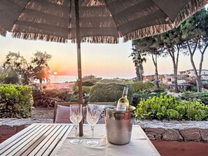 Ein Tisch im Freien mit einer Weinflasche, zwei Gläsern und einem Sonnenschirm, mit Blick auf eine schöne Aussicht auf das Meer und die Hügel.