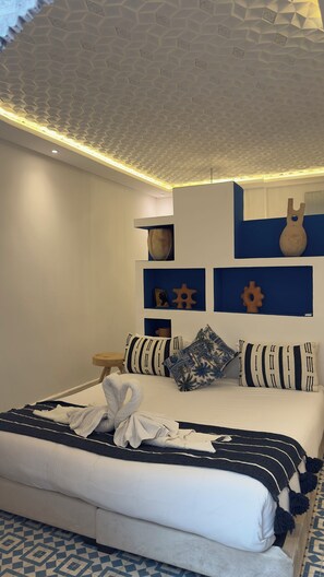 A modern bedroom with a geometric patterned ceiling, a neatly made bed with striped and floral pillows, and a blue and white patterned floor. - Fabulous 2-bedroom riad with AC in vibrant Marrakesh (Marrakesh)