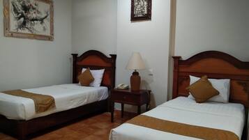 A hotel room with two single beds, a nightstand with a lamp, and two framed artworks on the walls.