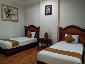 Quarto de hotel com duas camas de solteiro, uma mesinha de cabeceira com abajur e duas obras de arte emolduradas nas paredes.
