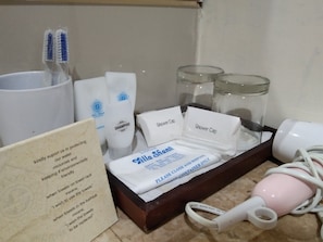 Casa de banho com dispensador de sabonete líquido, suporte para escova de dentes, frasco de vidro, touca de chuveiro, toalha e secador de cabelo.