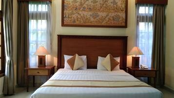 A hotel room with a large bed, two bedside tables with lamps, a painting above the bed, and curtains on the windows.