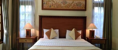 A hotel room with a large bed, two bedside tables with lamps, a painting above the bed, and curtains on the windows.