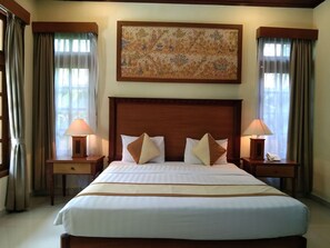 Quarto de hotel com uma cama grande, duas mesas de cabeceira com abajures, um quadro acima da cama e cortinas nas janelas.