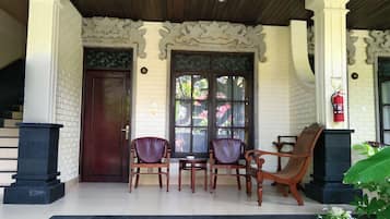 Un espacio de estar al aire libre cubierto con una mesa y sillas de madera, un extintor y un muro de ladrillo con detalles decorativos.