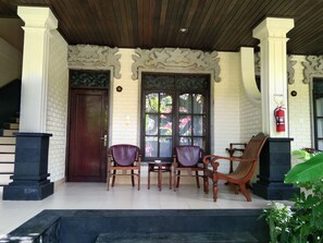 Un espacio de estar al aire libre cubierto con una mesa y sillas de madera, un extintor y un muro de ladrillo con detalles decorativos.